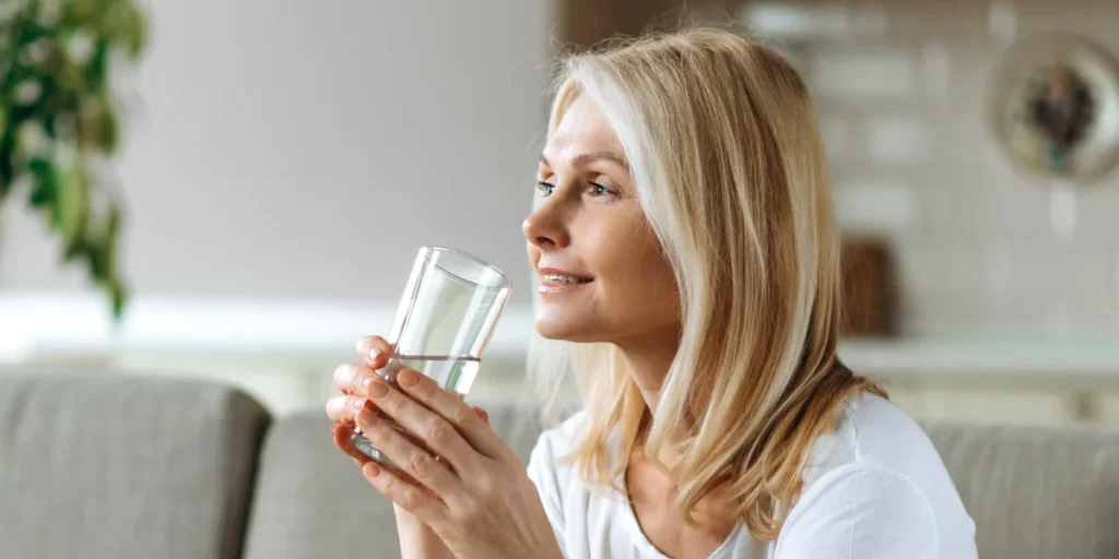 An older blonde woman of active age, holding a glass of water and looking forward to better days, has apparently just solved a problem—perhaps dry mouth—by using XyliDENT moisturizing lozenges or XyliDENT spray :) | Image source: shutterstock.com | For the article: What causes dry mouth and how to relieve it | For the website: healthchewinggum.com